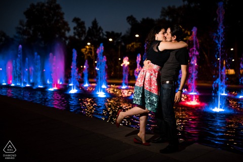In Mexico City, a couple poses at the fountains in a market plaza at night as he lifts her off the ground with one arm and they kiss, his other hand casually at his side, creating a striking and cool portrait.