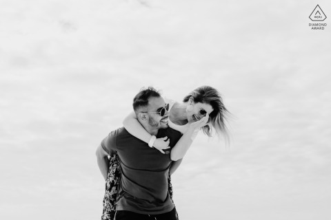 In Tulum, a woman smiles as she rides on her partner’s back for a playful, black-and-white portrait at the beach, set against a minimal backdrop of open sky.