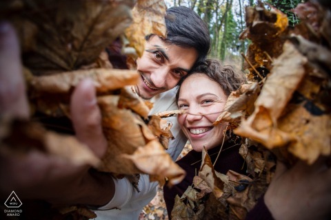 In Grenoble, France, a couple smiles for a wide-angle close-up portrait, holding dead leaves toward the camera.