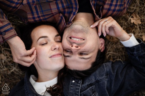 At Garden of the Gods in Colorado Springs, Colorado, an engaged couple lies on the ground in a yin-yang pose, gently stroking each other's faces, captured from a top-down view for their portrait.