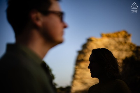 At Monument Rock in Monument, Colorado, an engaged couple poses for a creative portrait, with evening sunlight illuminating his face while his fiancée appears silhouetted against the rock formation.