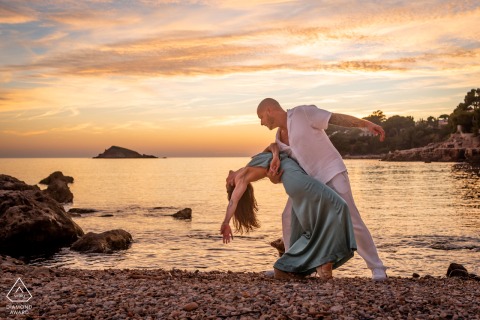 On a beach in Bandol, Var, Provence, France, a couple dances at sunset, posed in a romantic dip near the shoreline.