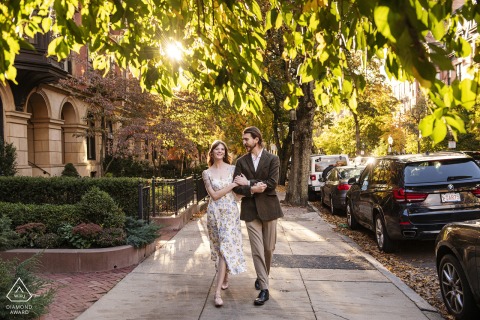 In Back Bay, Boston, Massachusetts, a couple walks arm in arm down a sidewalk, center framed with sunlight filtering through the trees behind them.