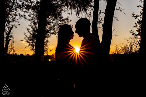 In Parque Villarino, Argentina, a couple poses in silhouette during a wedding pre-session, their profiles outlined by a sunburst effect created with a photographic filter.