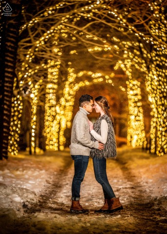 On Addison Street in Philadelphia, a couple stands nose to nose in profile for a night portrait, with snowflakes falling and sparkling lights in the background.