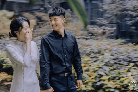A couple holding hands walks briskly past the Hua Yue International Hotel in Kaifeng, China, sharing a warm smile as they glance at each other.