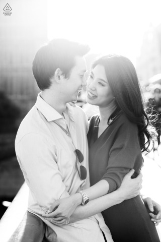 Couple standing together in a tall vertical black and white portrait, with the sun glowing brightly behind them, casting a dramatic backlight and highlighting them in London.