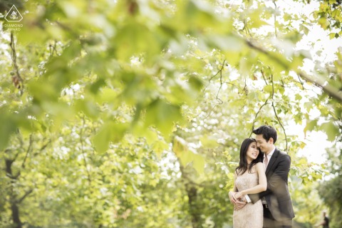 Couple embracing under a lush canopy of green foliage in London, England, surrounded by vibrant trees, their affectionate connection highlighted beneath the peaceful, shaded scene.