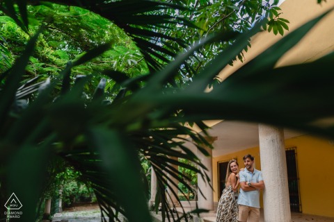 Couple leans together against weathered porch columns of an abandoned colonial house in Valladolid, Yucatan, evoking a sense of romance amid the timeless, historic architecture.