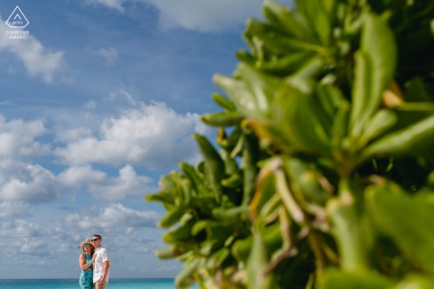 At Cancun’s Playa Delfines, a couple is artistically framed off center beneath vibrant sky and tropical leaves, with the bold blue sky creating a dramatic and visually striking portrait.