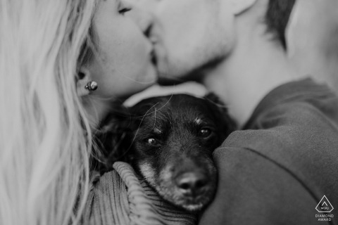 Tender Kiss Frames Dog’s Calm Gaze In Black And White Hungary Portrait, Celebrating Deep Bonds And Pure Closeness In this black and white portrait from Hungary, a couple’s tender kiss frames their dog’s calm gaze, capturing a scene of pure closeness and the deep bonds they share.