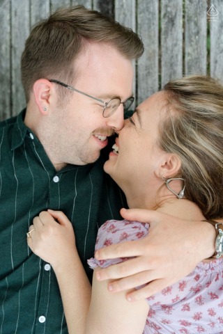 Couple lying together on a picnic table by the coast in Brooklin, Maine, sharing a joyful laugh as the ocean breeze enhance their playful engagement session.