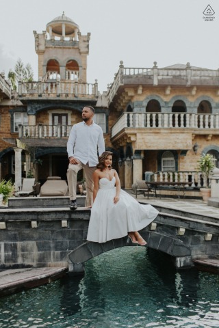 Couple poses together on a stone bridge over water at a private residence in Freeport, Trinidad, with a castle-like old world building towering behind them.