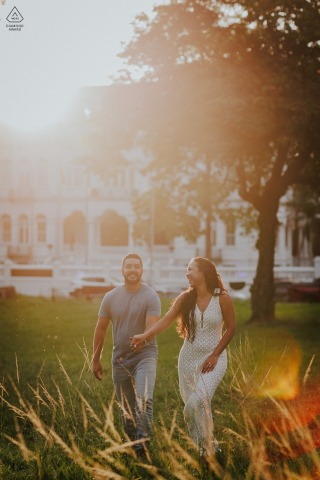 Engagement shoot at Queen's Park Savannah, Trinidad, with the couple walking hand in hand, beautifully backlit by the intense golden hour sun, creating a warm and romantic atmosphere.