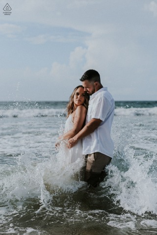 Engagement shoot at Las Cuevas Beach, North Coast Trinidad, features a couple embraced in the ocean as waves crash around them, capturing the romance and excitement of the session.