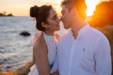 Close and intimate, the couple leans toward each other at The Knob in Falmouth, MA as the sun sets over Cape Cod, warm highlights and soft light emphasizing their genuine connection.