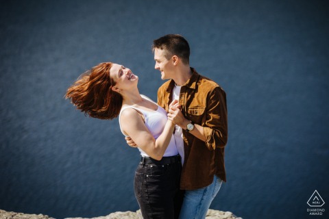 Couple joyfully swings each other around in the Catskills, New York, with hair flying in the wind, capturing a playful and energetic engagement portrait amidst natural, scenic beauty.