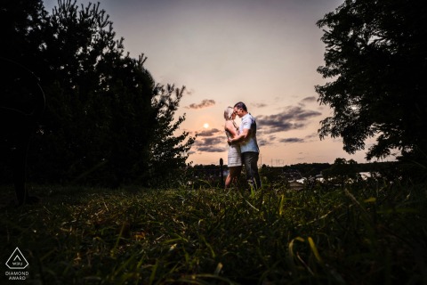A couple holds each other on a grassy hill at Fairmount Waterworks in Philadelphia, center framed and backlit by the setting sun, creating a warm and intimate portrait.