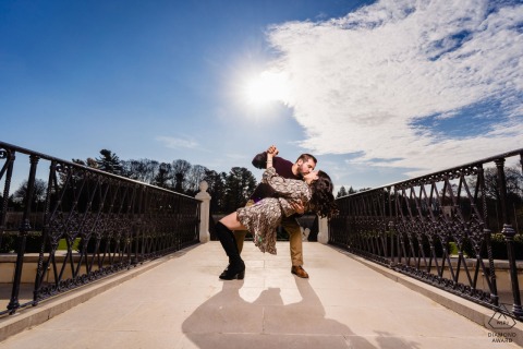 He gently dips her on a bridge at Longwood Gardens in Philadelphia as they share a kiss, with open skies and bright afternoon light adding warmth to this affectionate and fun portrait.