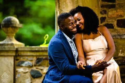 The couple sits close against a stone wall in Ridley Creek State Park, smiling easily as the peaceful atmosphere of the park surrounds them in this relaxed, intimate portrait.