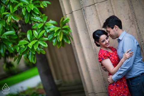 Engagement portrait of a couple standing and embracing beside enormous, ribbed stone columns of an old world building in San Francisco, wrapped in a loving embrace.