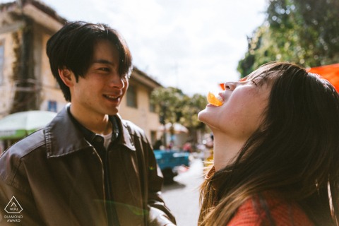 Couple enjoying a snack at a bustling Yunnan farmer’s market, both smiling as the woman tilts her head back with happiness among vendors.
