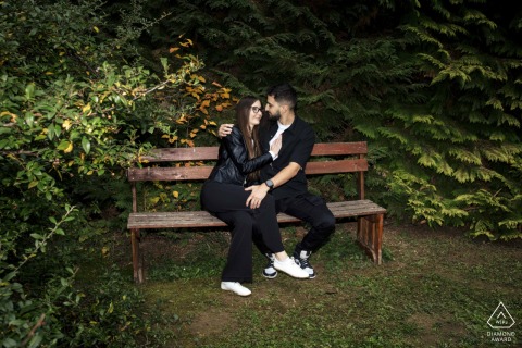 On A Quiet Bench In Budakeszi The Couple Sits Close Together While Sharing Meaningful Looks On a quiet bench surrounded by lush greenery in Budakeszi, the couple sits close together while sharing a soft, meaningful look that expresses their deep devotion during their engagement.