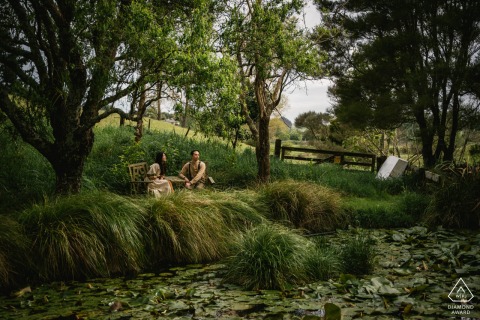 A couple sits chatting quietly in front of a serene lake covered in lilies in Wanaka, New Zealand, finding a peaceful and private connection in the beautiful outdoors.