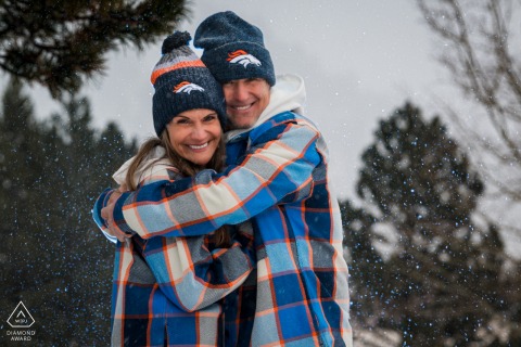 Denver Broncos Fans Wear Team Outfits For Snowy Winter Engagement Portrait In Estes Park Colorado Dedicated Denver Broncos fans wear their team outfits for a snowy engagement portrait in Rocky Mountain National Park, Estes Park, Colorado, celebrating their love amidst the winter mountain landscape.