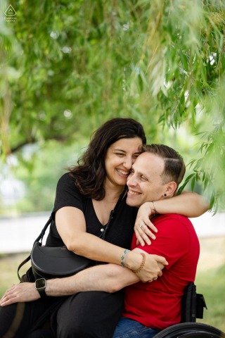 Nestled under the sweeping branches of a willow tree in the Old Port of Montreal, Quebec, an engaged couple shares a warm and intimate hug during their romantic photoshoot.