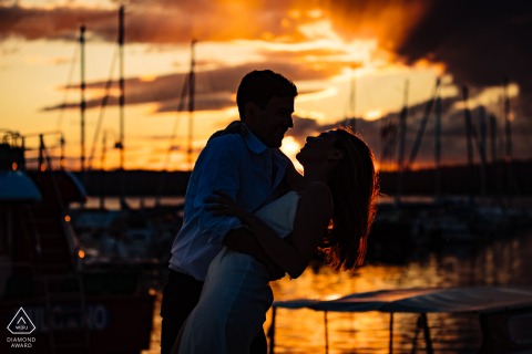 A beautiful couple is framed by the glowing colors of a sunset on the lake at Lago di Bolsena, Italy, highlighting their romantic engagement in the heart of Tuscany.