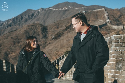 The couple stands together against the historic stone architecture of the Mutianyu Great Wall in Beijing, China, representing an enduring love that spans through time at this iconic landmark.