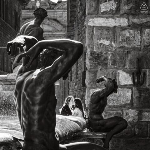 Two lovers are framed poetically by the sculptures of the Fountain of Neptune in Piazza della Signoria, Florence, Italy, creating a striking contrast between their intimacy and the statues.