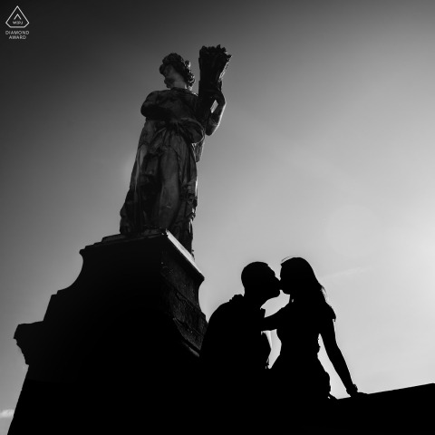 Framed by the dark silhouette of a historic statue in Florence, Italy, a couple shares a tender kiss against the fading daylight, celebrating their love beneath the gaze of history.