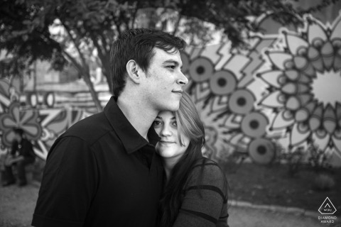 An engaged couple is seen warmly hugged up in front of a mural in the Cabbagetown neighborhood of Atlanta, Georgia, showcasing their love in an artistic urban setting.