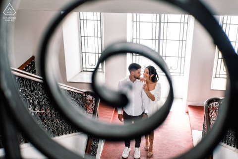 Seen through the intricate details of a grand staircase, the couple shares a meaningful look during their sophisticated engagement portrait session at the historic Palácio Deodoro in Alagoas, Brazil.
