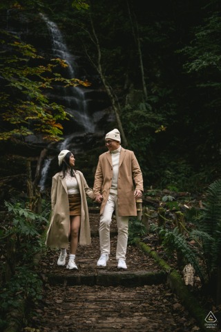 The couple walks hand in hand in front of a cascading waterfall in Aomori, Japan, their relaxed steps and shared glances complemented by the natural power and tranquility of the rushing water behind them.