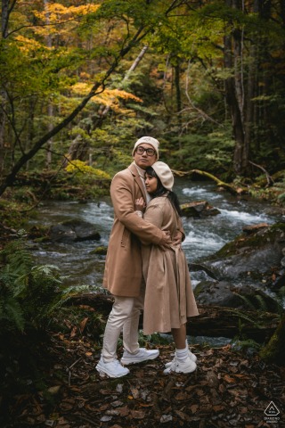 In Aomori, Japan, the couple poses in the forest during the vibrant fall season, colorful leaves carpeting the ground and overhead branches, their connection highlighted by the beauty of nature’s changing colors.