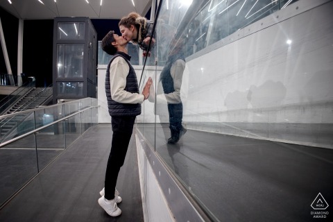 In Grenoble, France, a couple shares a kiss against the city’s urban backdrop, the surrounding architecture and natural light adding to the intimate nature of their engagement portrait.