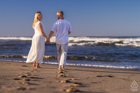On Newcomb Hollow Beach in Wellfleet, Massachusetts, the couple strolls along the shoreline, the bride glancing back with an unguarded smile as the gentle waves frame their easygoing romance at this scenic beach venue.
