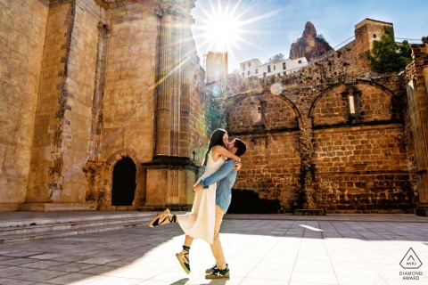 At Iglesia de Santa María in Cazorla, Jaén, Spain, he lifts her in a romantic gesture, sunlight bursting behind them as they’re framed by the historic stone buildings, their smiles illuminated against the old world backdrop.