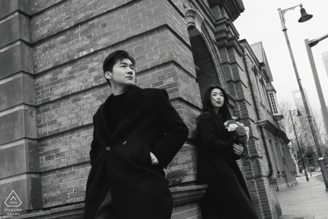 A black-and-white portrait of a couple in Shanghai, leaning against the Bund’s historic brick wall, their engagement portrait reflecting quiet confidence amid the city’s timeless architecture.