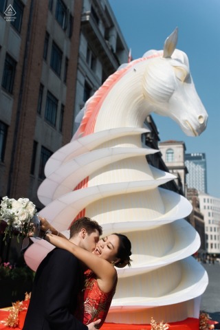 Beneath the white horse in Shanghai’s Bund, a couple shares a kiss, their engagement portrait framed by the symbolism of the Year of the Horse and the surrounding historic area.