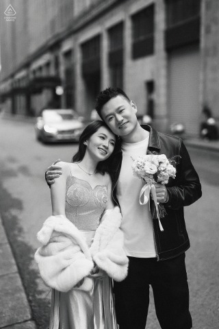 In Shanghai’s Bund, a couple leans into each other, her bouquet held by him as they pose for a straightforward engagement portrait with the city streets behind them.