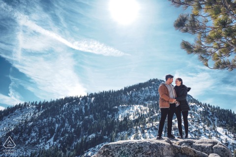 The couple stand hand in hand in South Lake Tahoe, California, mountains and water creating a breathtaking natural backdrop for their joyful engagement portrait session.