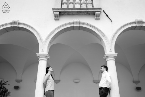 A couple stands close beneath elegant stone arches in Slovenia, soft light falling across the architecture as they pose together for a romantic engagement portrait surrounded by timeless European charm.