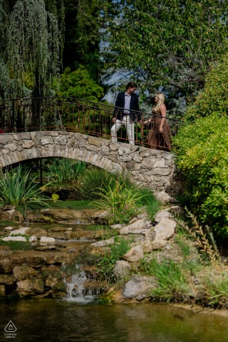 On a stone bridge above a stream at Chateau de Berne in Provence, a couple stands together, surrounded by lush greenery, their engagement portrait highlighting the serenity of the garden setting.