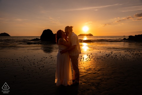 On a beach in Quepos, Costa Rica, a couple hugs at sunset, captured in an engagement portrait emphasizing intimacy and the warm evening light.