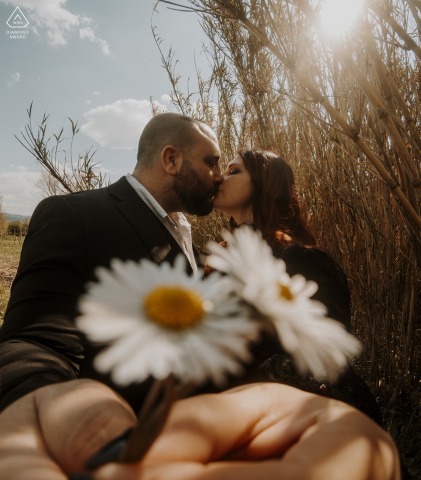 In Ceparana, Liguria, Italy, a couple is photographed among flowers in an engagement portrait, with floral elements incorporated into the composition to frame their interaction.