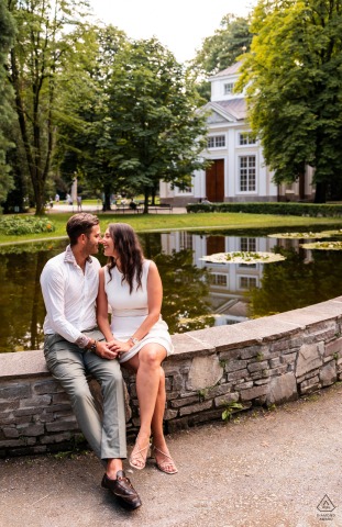 Couple Sitting Together By Pond In Tranquil Innsbruck, Austria Portrait From Engagement Photographer’s Session In Innsbruck, Austria, a couple sits together at the edge of a pond, captured in a calm and intimate engagement portrait with soft afternoon light.